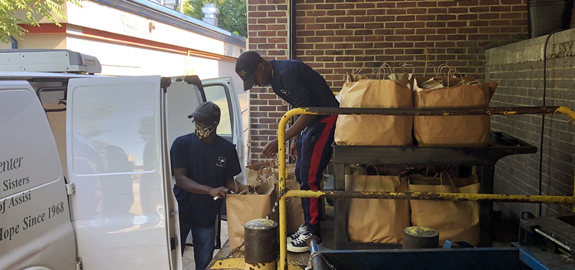 Two male employees loading delivery van with meal packs. 